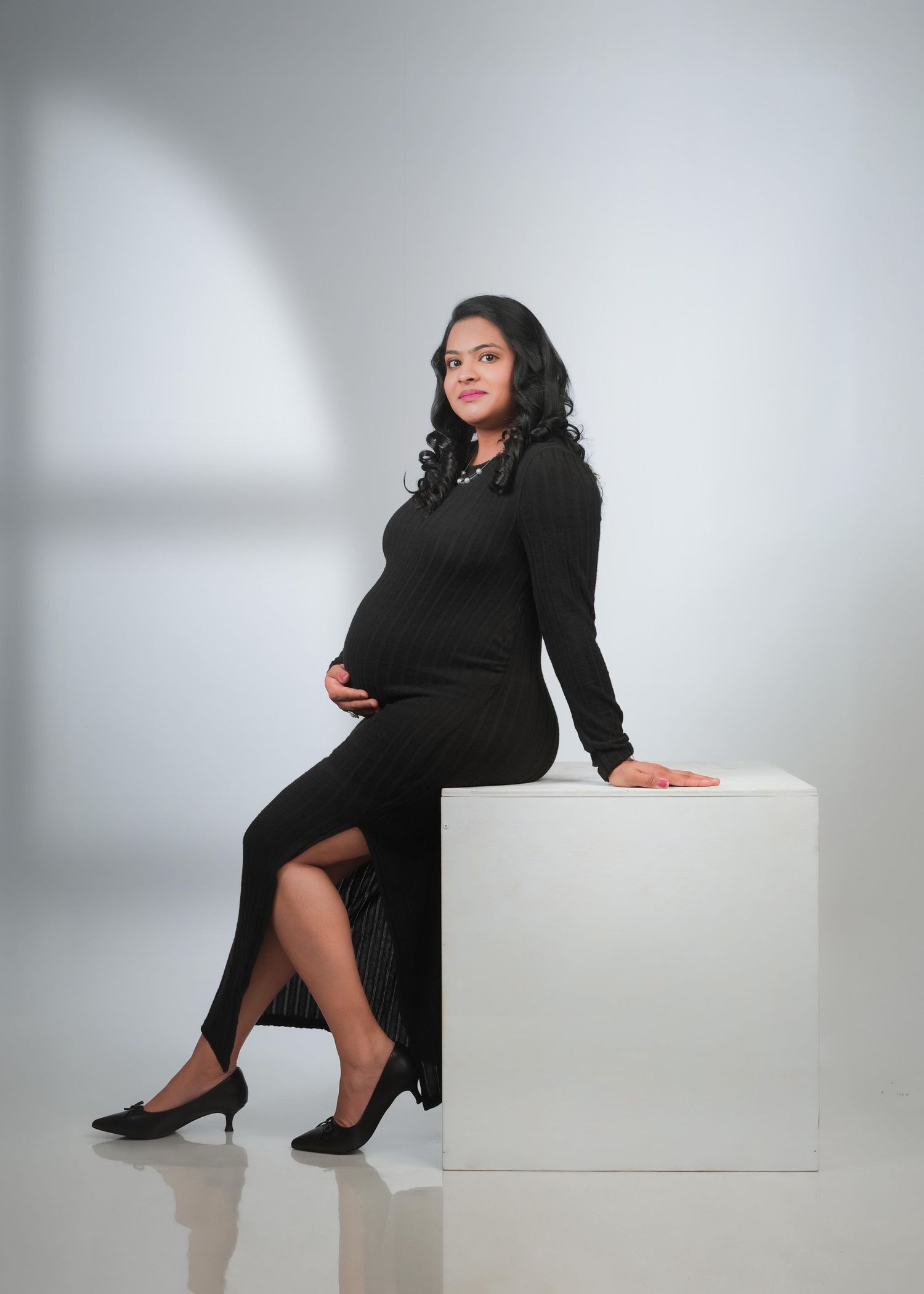 Elegant maternity studio photos in black dress against white background.