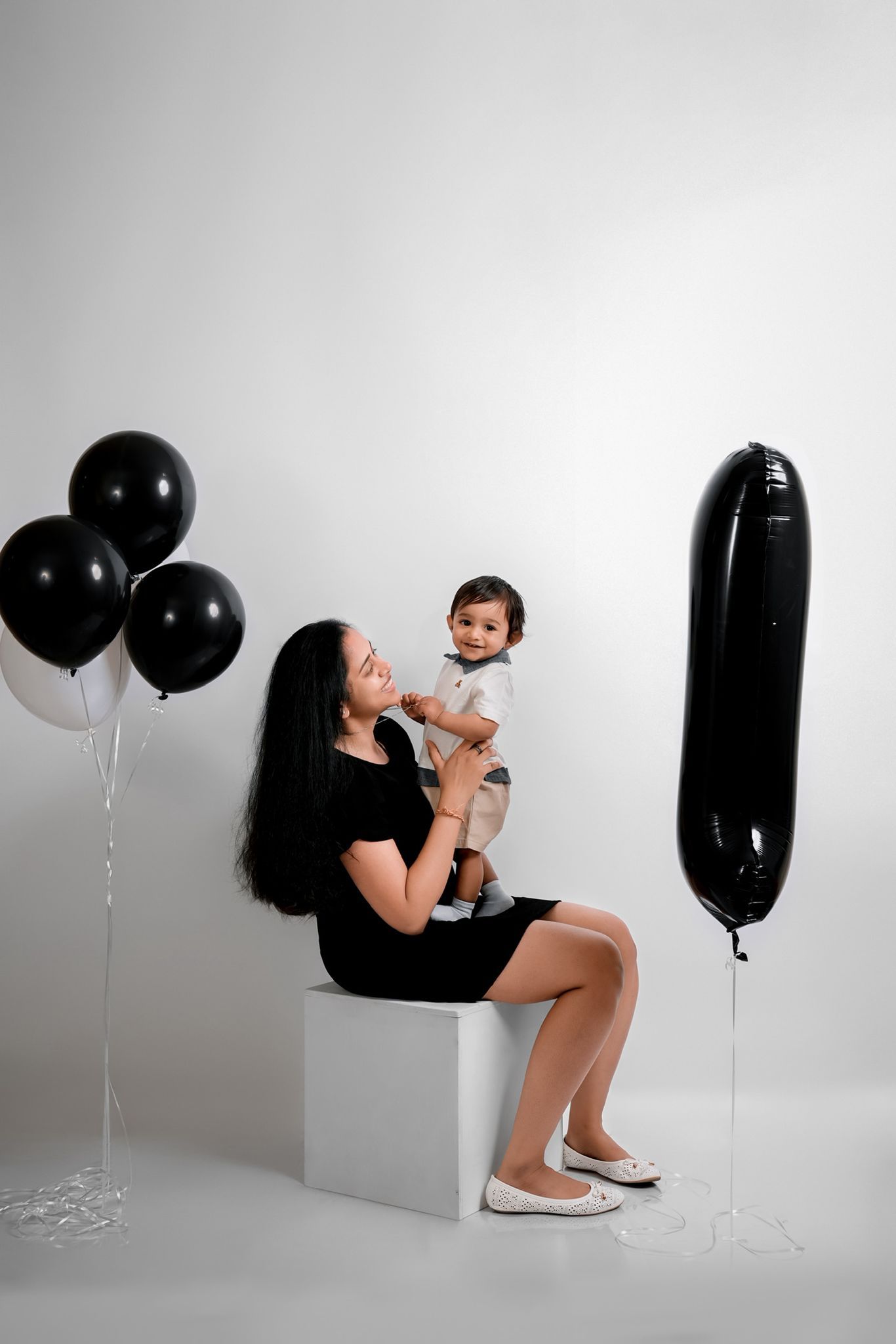 Studio photoshoot featuring black and white balloon decor and minimalist white blocks as props.
