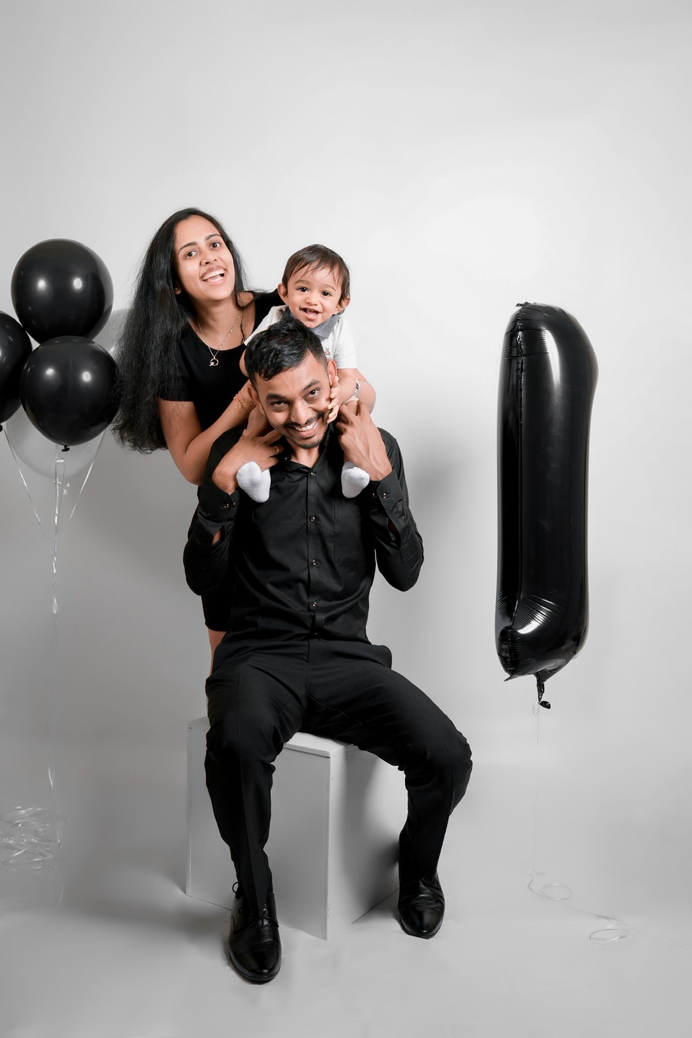 Family photoshoot featuring black balloons and white cube in minimalist setting.
