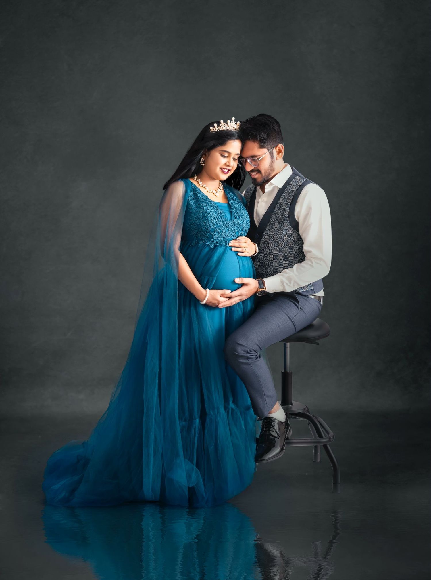 Intimate maternity portrait with couple in blue gown against dark backdrop.