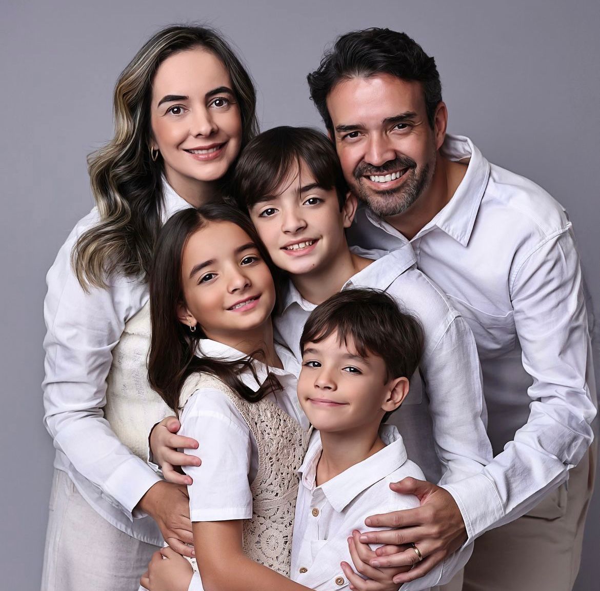 Studio portrait of family group wearing coordinated white outfits against grey background.