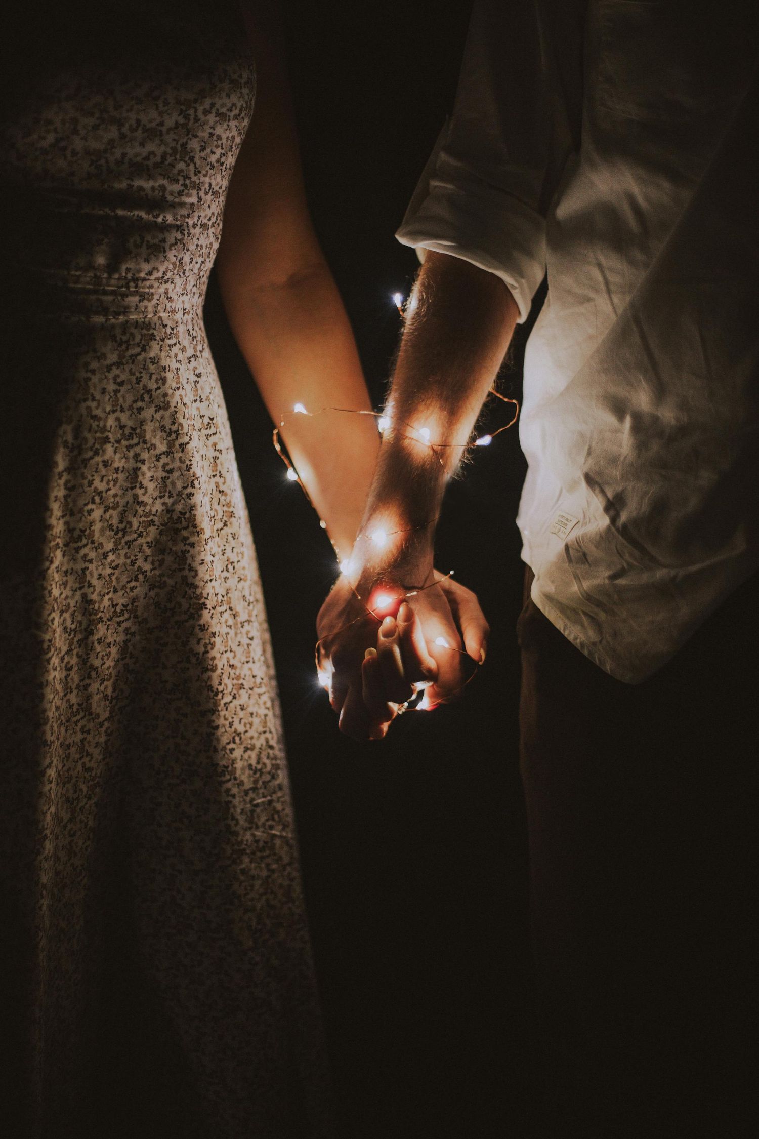 Hands holding sparklers create magical light trails in dark setting.