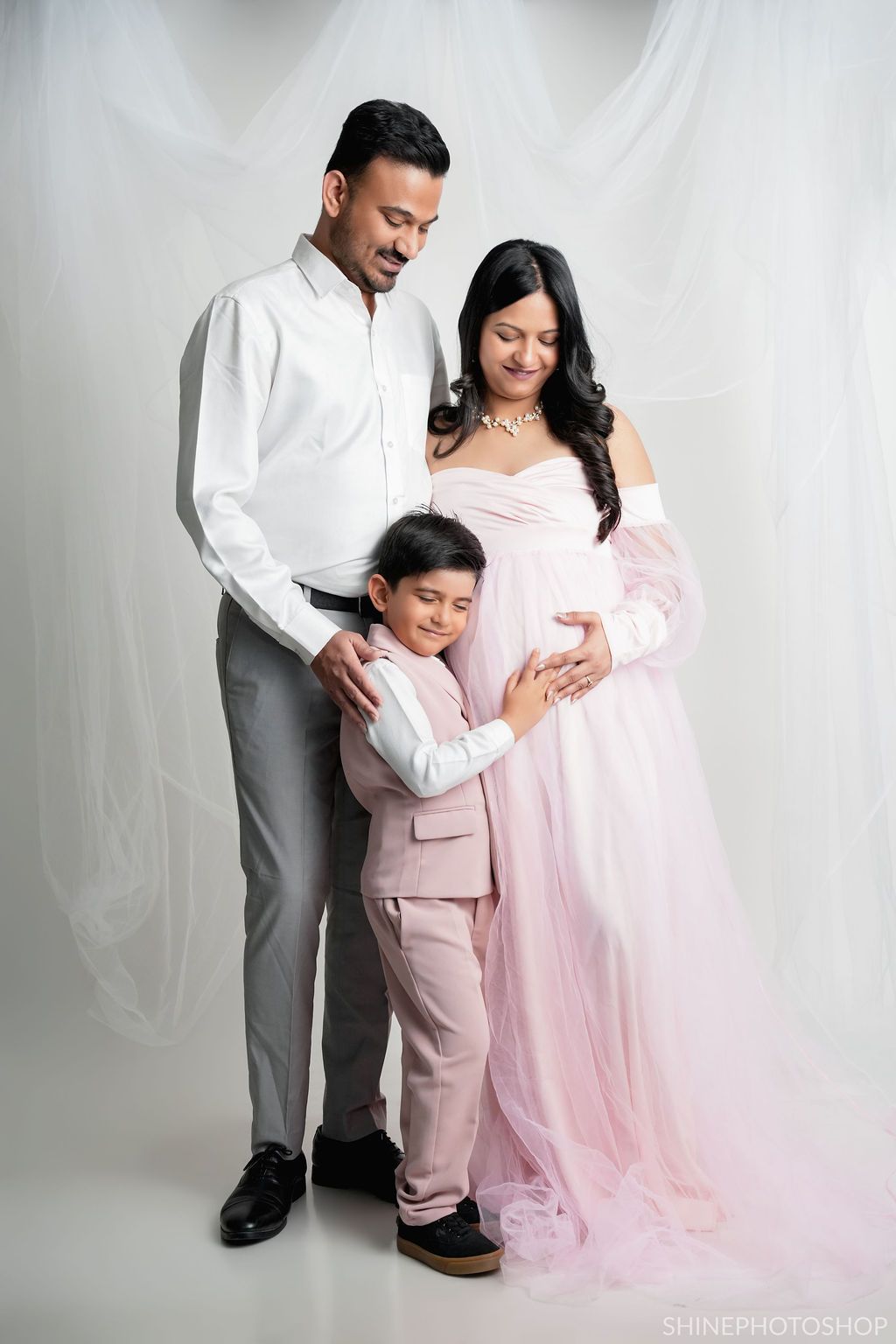 Family maternity portrait in pink and white outfits against clean studio backdrop.