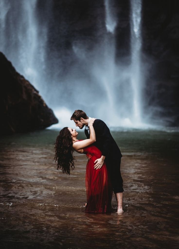 A romantic couple poses dramatically near a misty waterfall in an artistic photoshoot sequence.