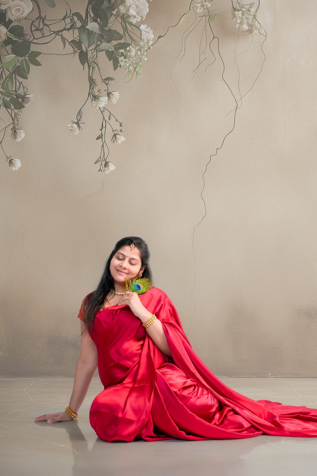 Maternity photos with floral decor showing graceful poses in a vibrant red gown against a beige wall.