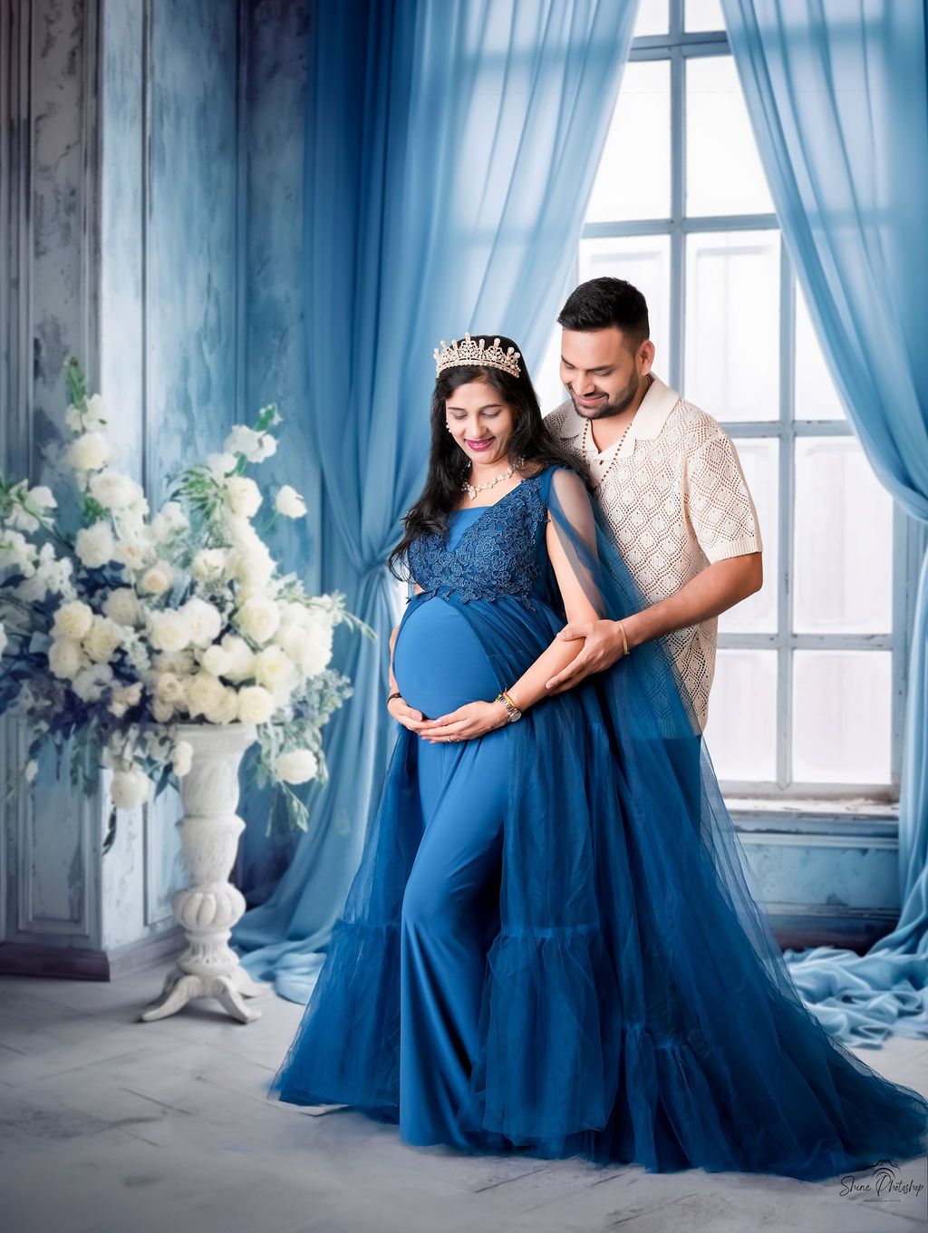 Maternity portrait in royal blue gown with flowing tulle against blue-toned romantic setting.