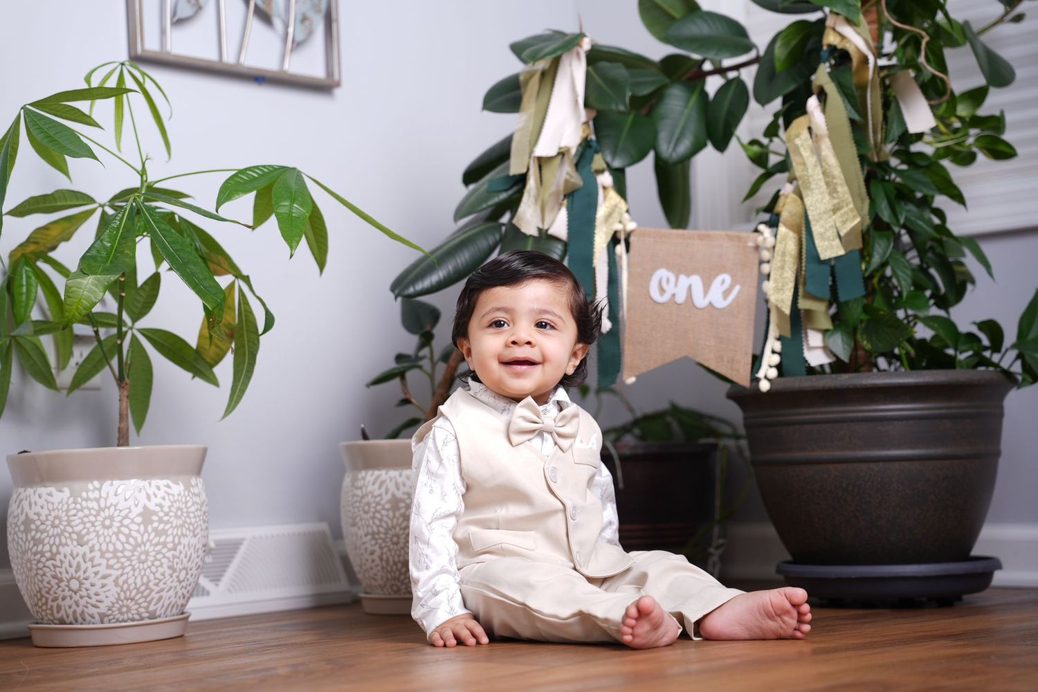 Indoor photoshoot setup with potted plants and 'one' sign decoration.