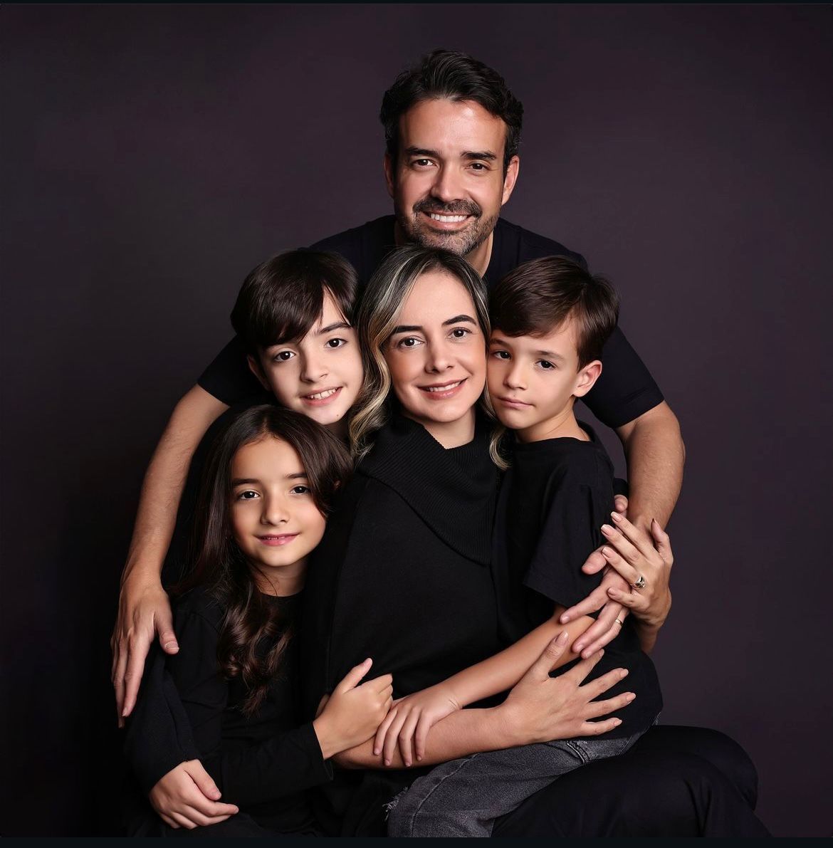 Studio family portrait session with everyone wearing black against dark backdrop.