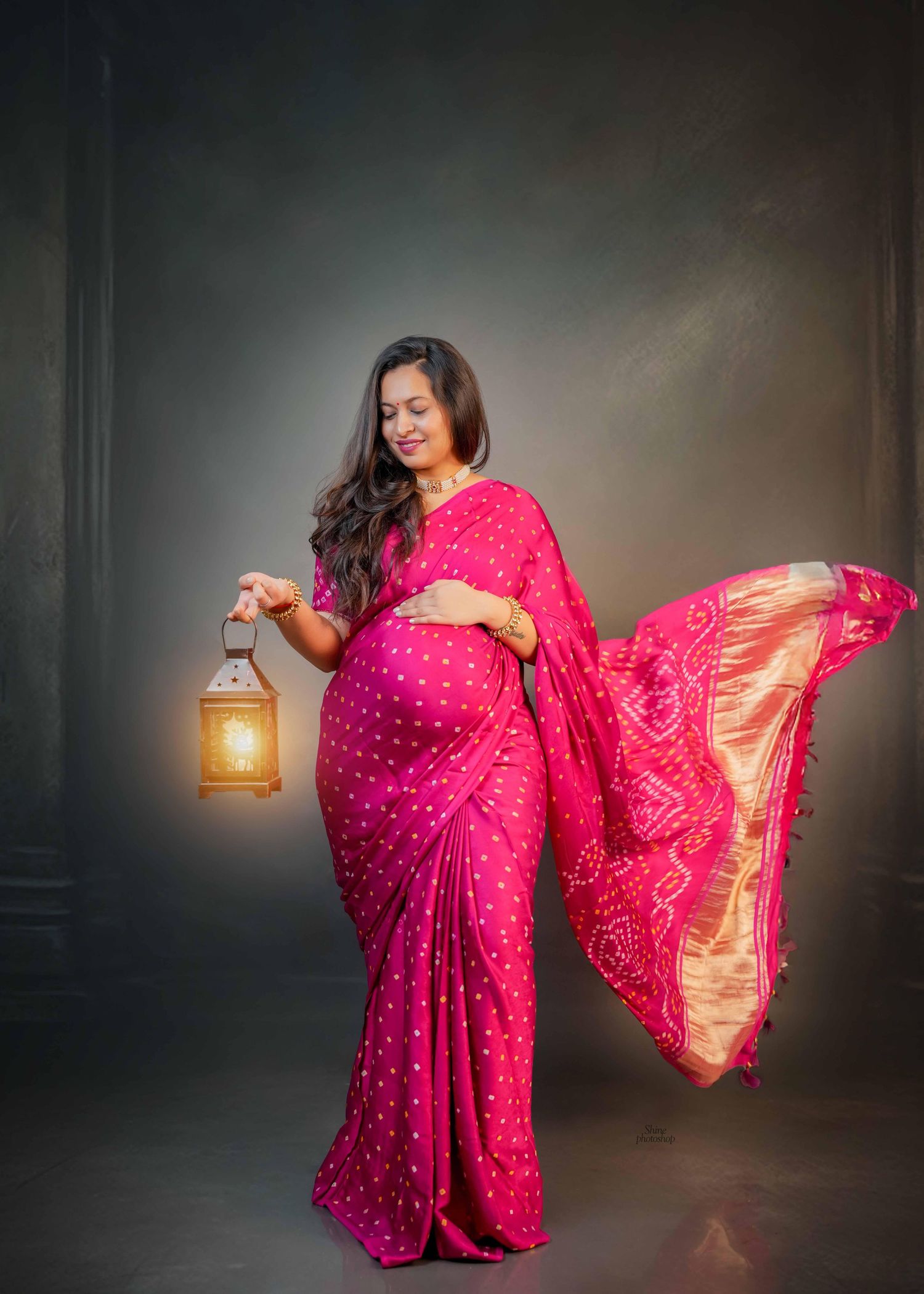 Vibrant pink and gold sari-inspired maternity photoshoot with dramatic lighting and flowing fabric.