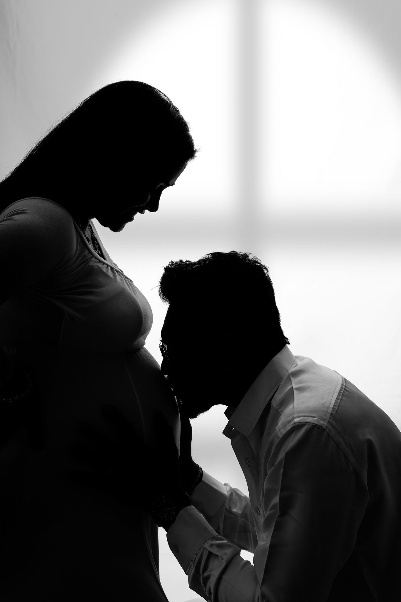 Silhouette of intimate pregnancy moment in black and white with dramatic lighting.