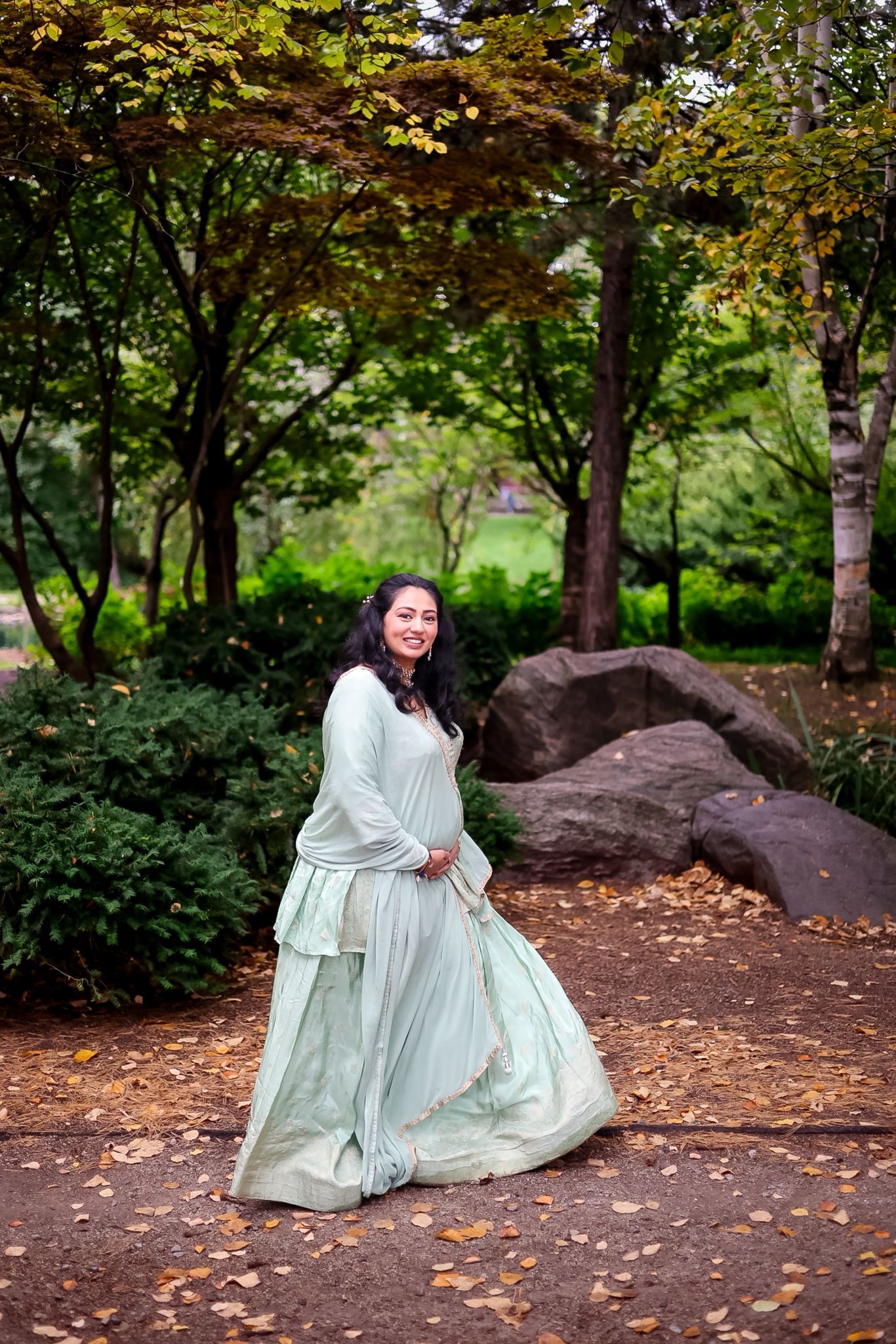 A woman in a flowing mint green dress poses gracefully in an autumn garden setting.