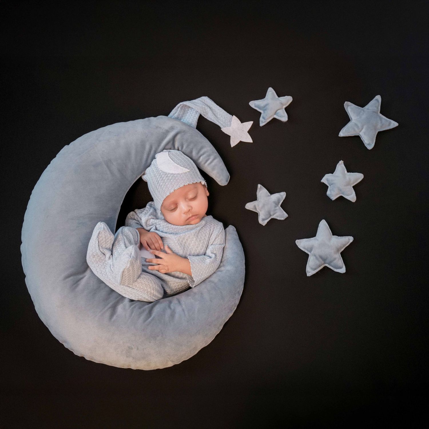 Minimalist newborn photography setup with silver stars against dark background.