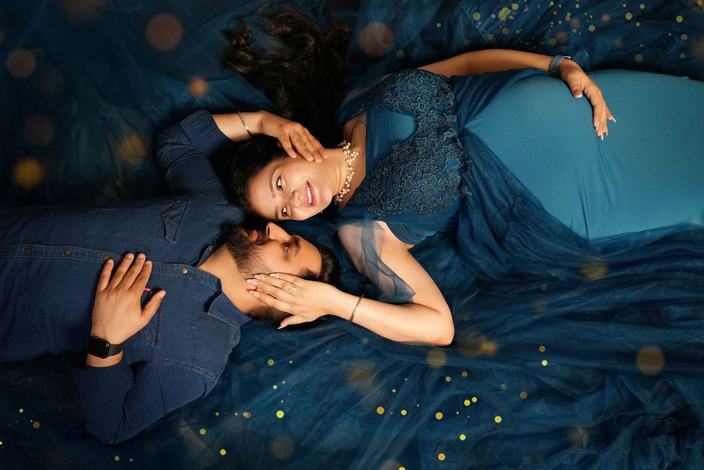 Couple in matching navy blue outfits pose lying down with magical bokeh lighting effects.