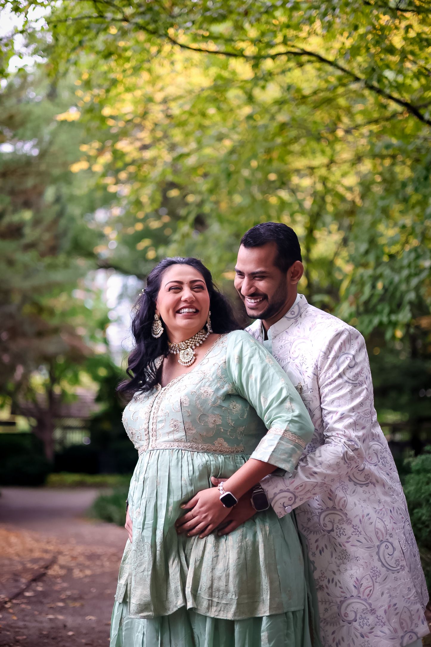 A couple shares joyful moments in coordinated mint green and white outfits under autumn trees.