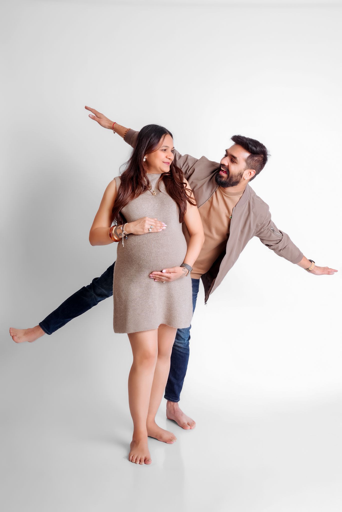 Playful maternity pose with couple pretending to fly against white background.