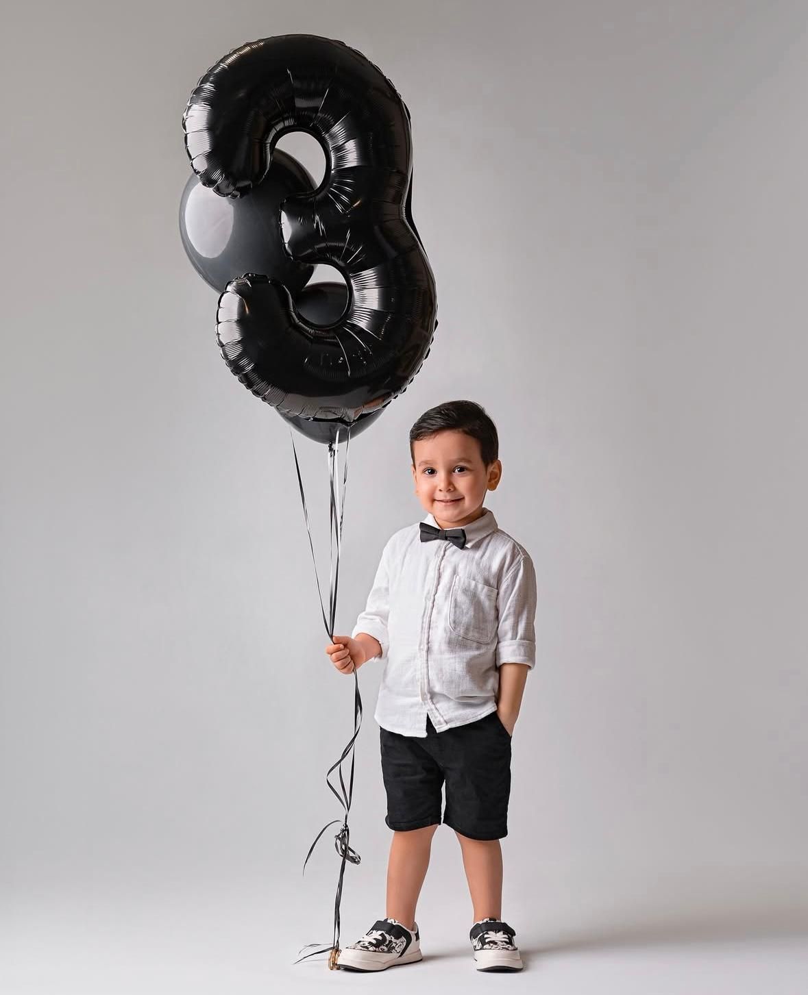 Black balloon photoshoot with child in formal attire.