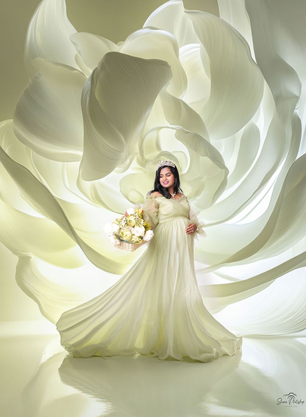 Ethereal white maternity gown photographed against a soft white rose petal backdrop.