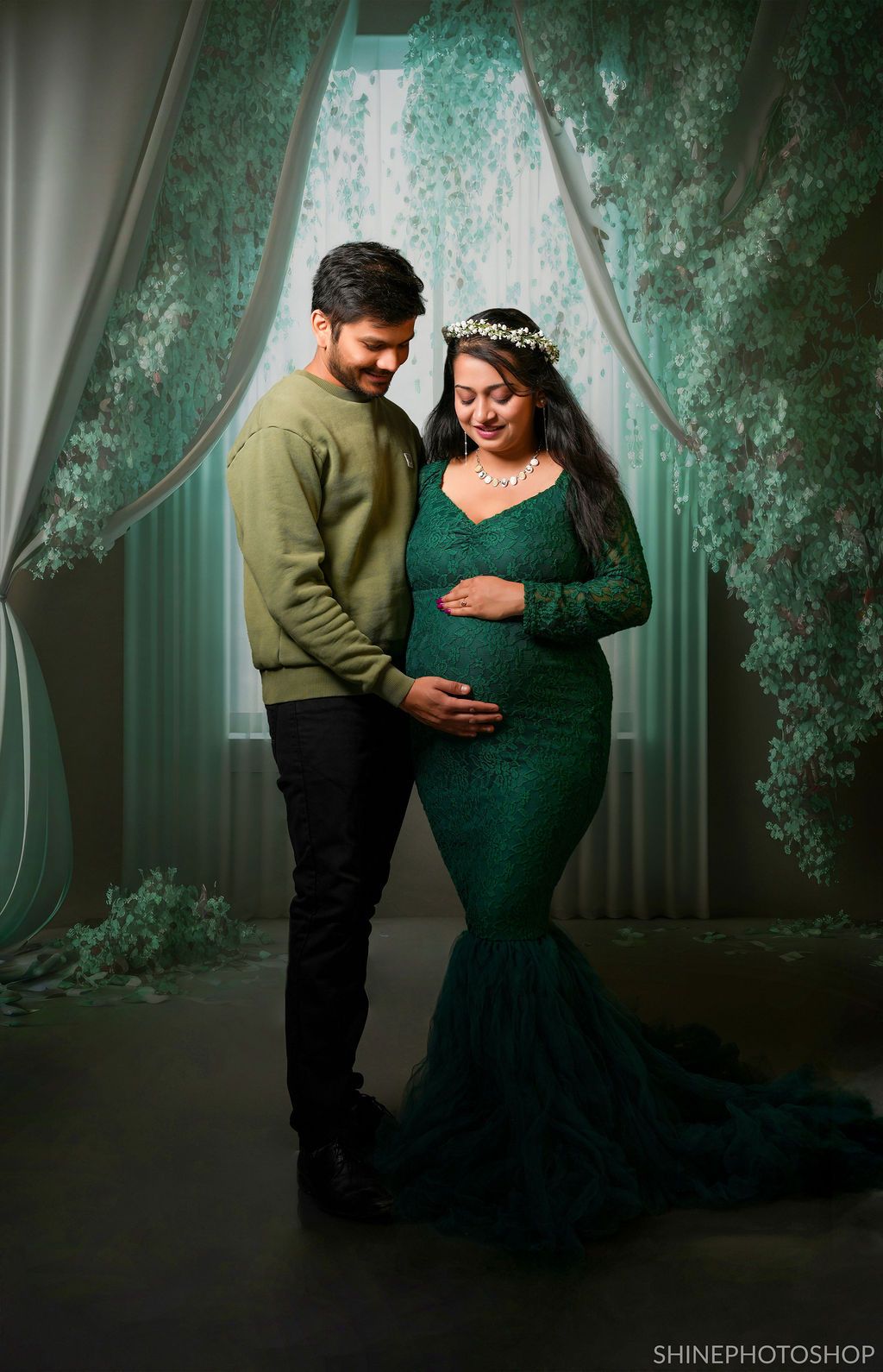 Intimate maternity portrait with emerald lace gown in moody green lighting.