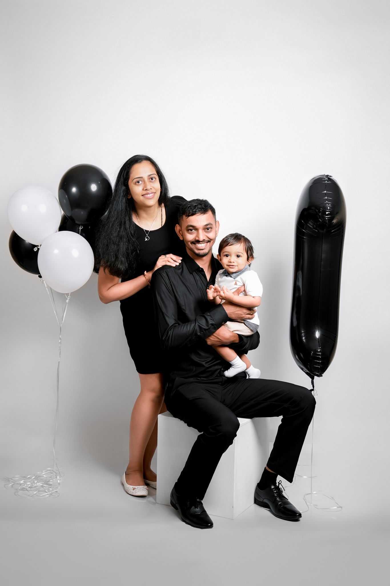 Family poses together in coordinated black outfits with monochrome balloon decorations in studio setting.