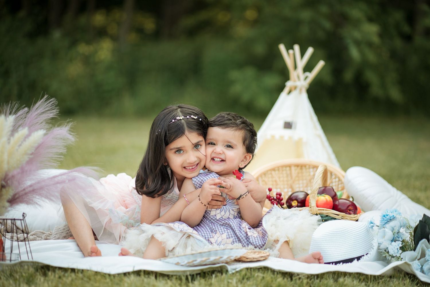 Dreamy outdoor picnic setup with soft pink decor and blankets on grass.