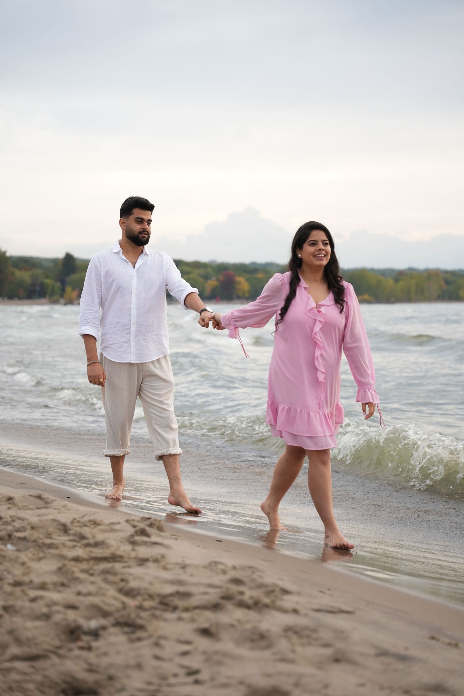 A couple walks along a sandy beach wearing casual pink and white outfits.