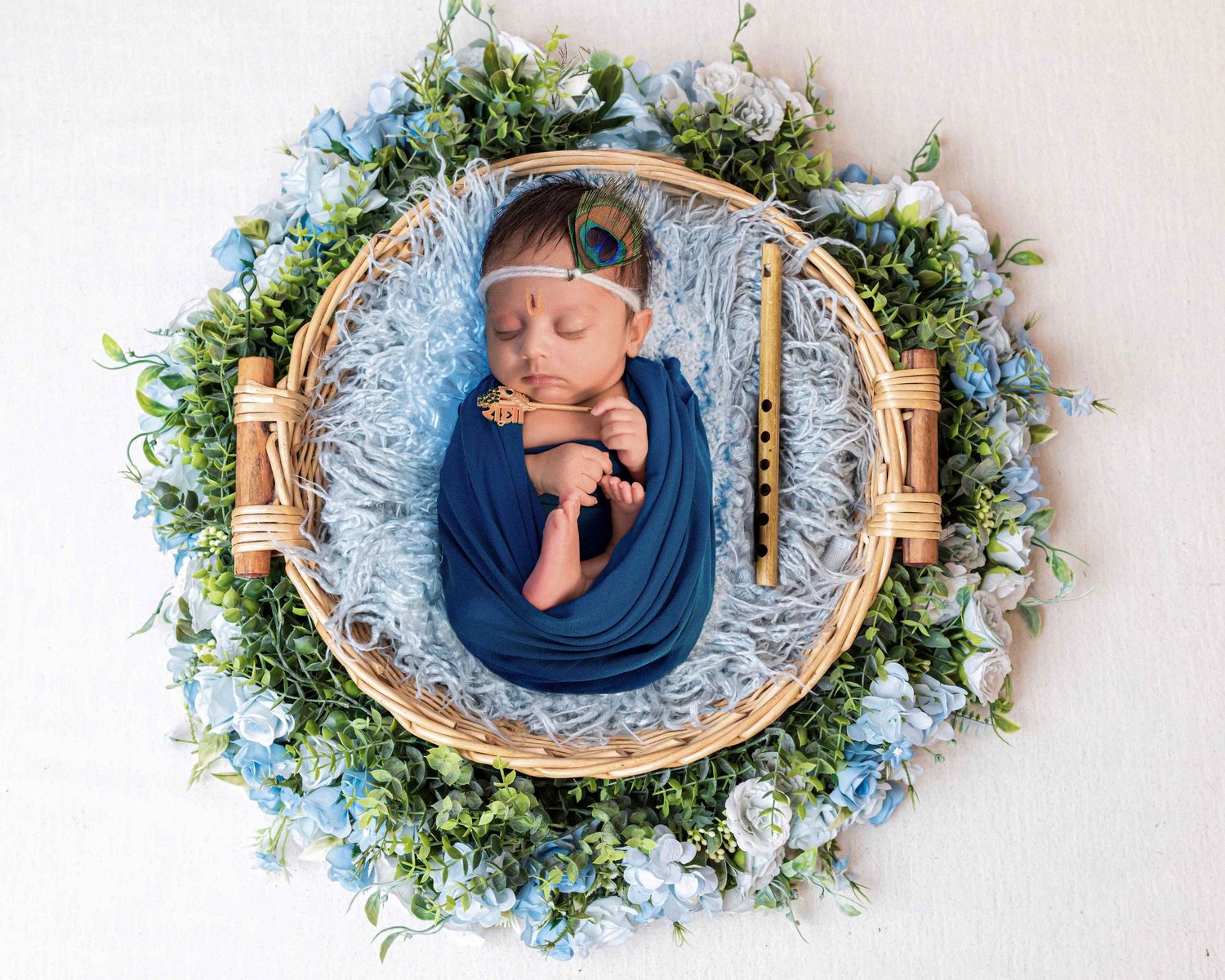 Floral wreath basket surrounded by blue flowers creates dreamy newborn photography scene.