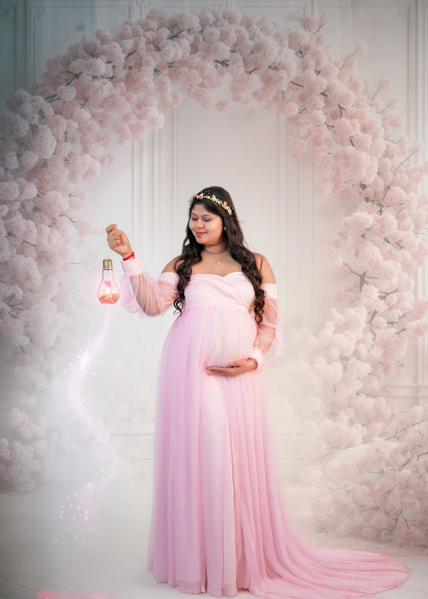 Ethereal maternity portraits in a flowing pink gown surrounded by cherry blossoms.