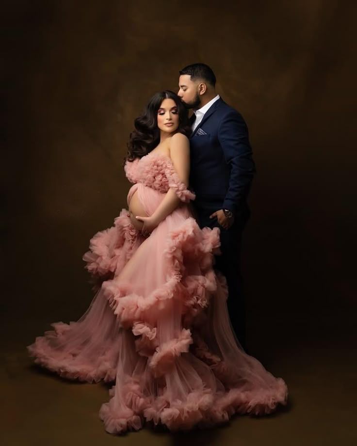Romantic couple's maternity portraits featuring a flowing dusty rose gown against dark background.