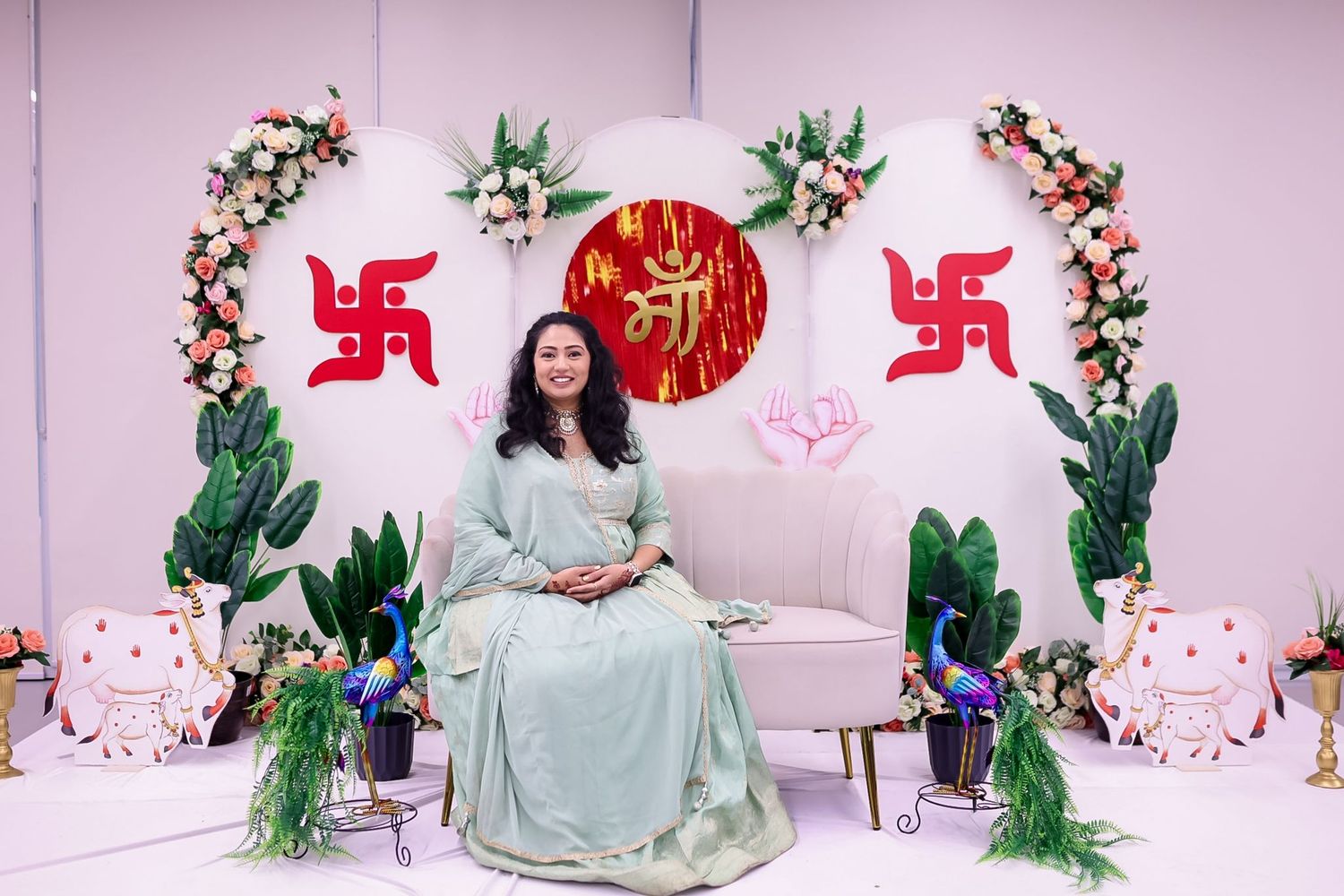 Baby shower setup with floral decorations and traditional Hindu symbols against pink backdrop.