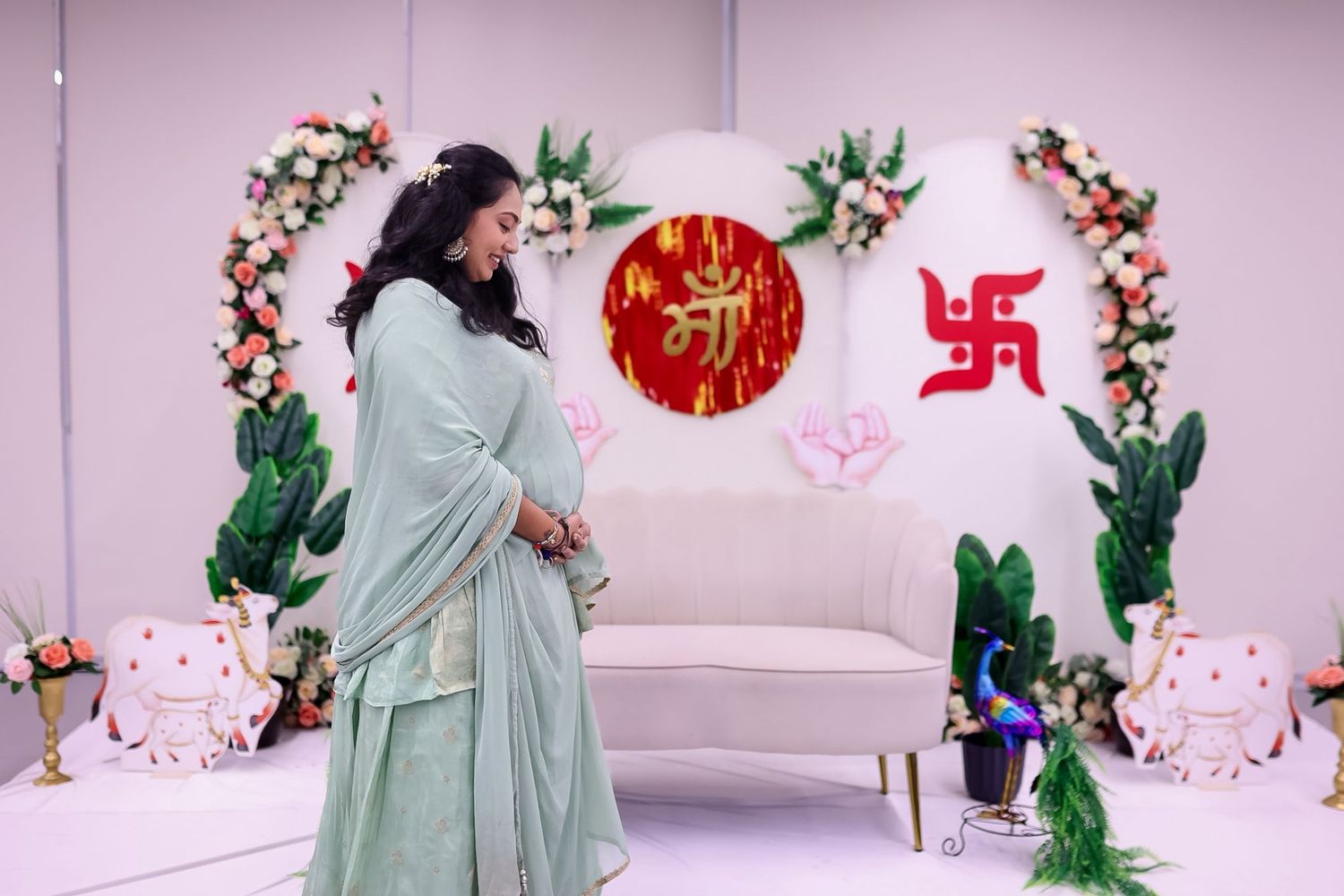 Maternity celebration with couple posing against pink wall adorned with flowers and religious symbols.
