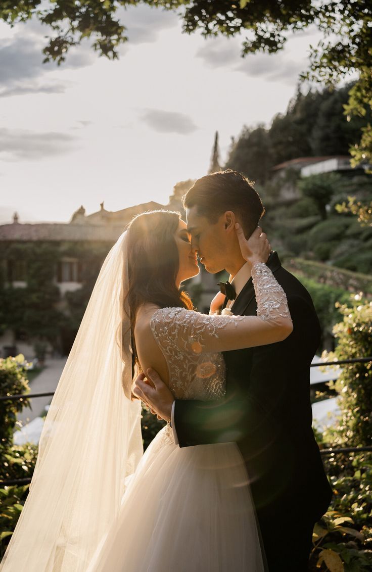 Wedding couple embracing in golden sunlight with trees and a flowing veil creating a romantic silhouette.