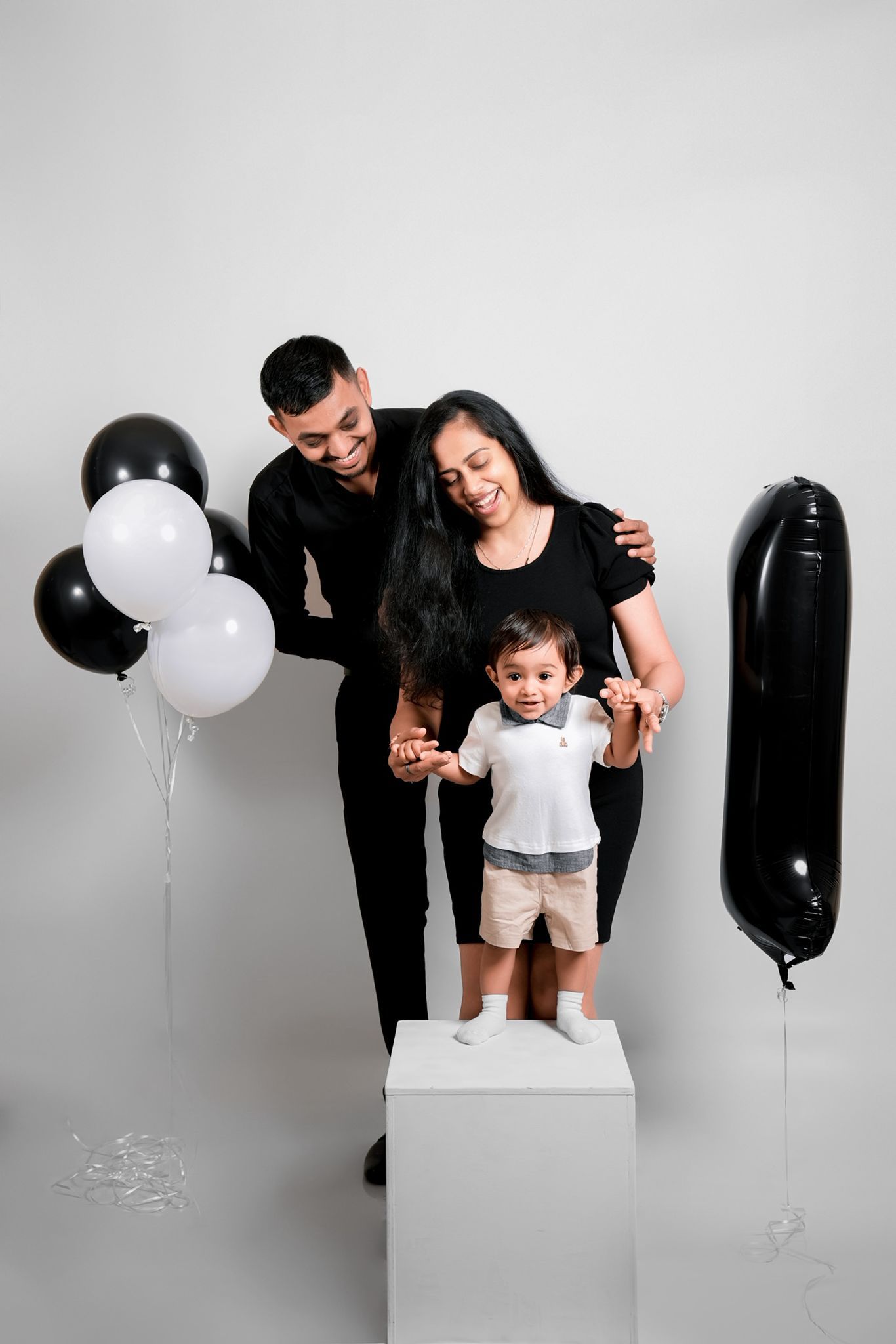 Studio family session with black and white balloons against light backdrop.