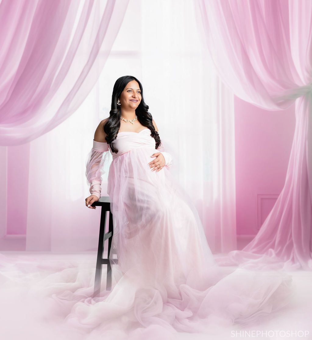 Romantic maternity photo with soft pink drapery and ethereal lighting.