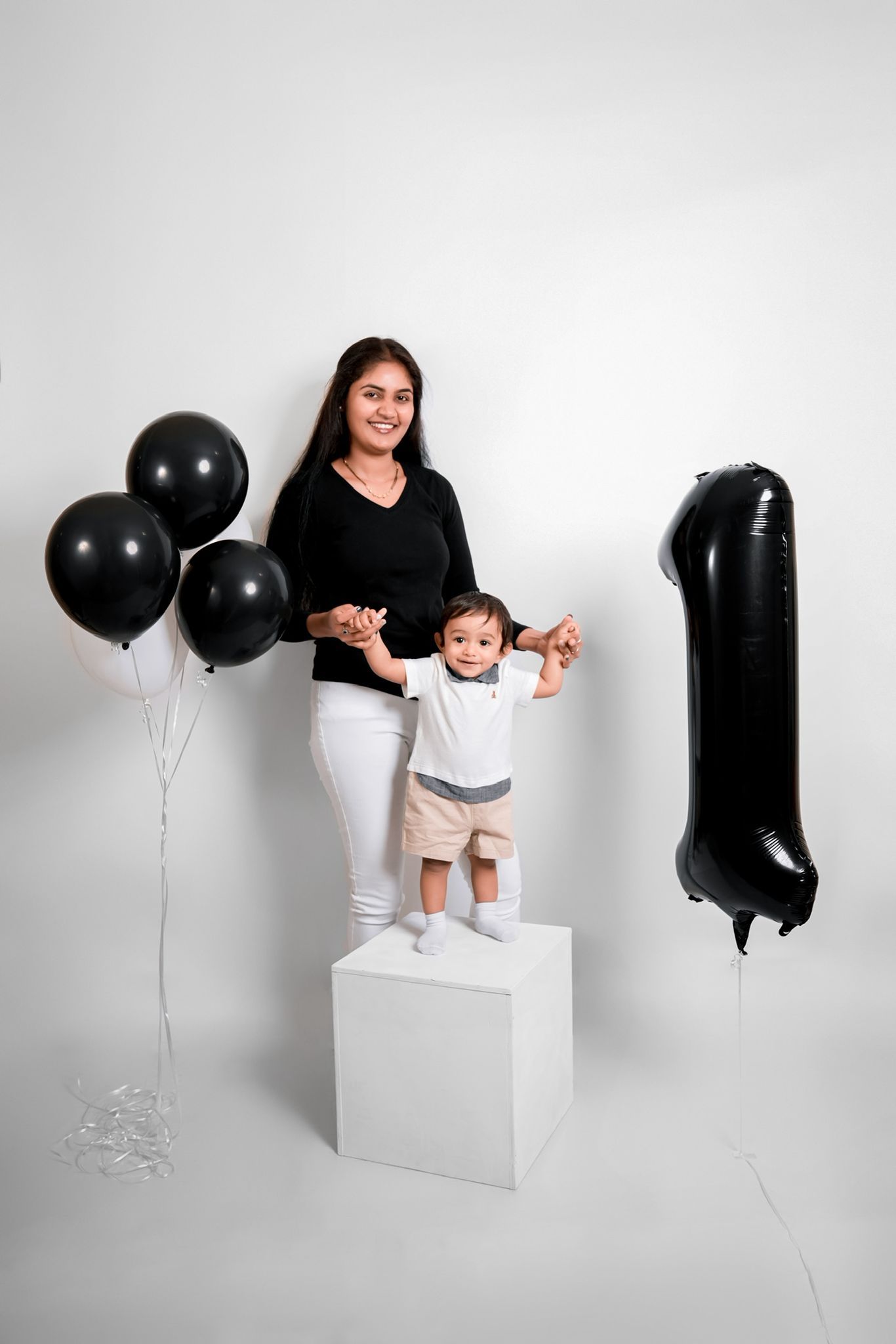Studio photoshoot with black balloons and white cube against light background.