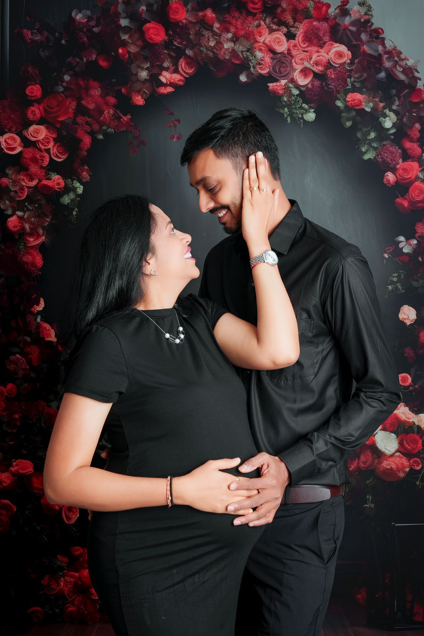 A romantic couple in black attire shares intimate moments against a dark backdrop with red roses.