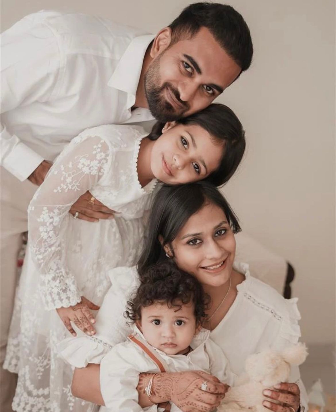 Family in white outfits sharing loving moments against a neutral backdrop.