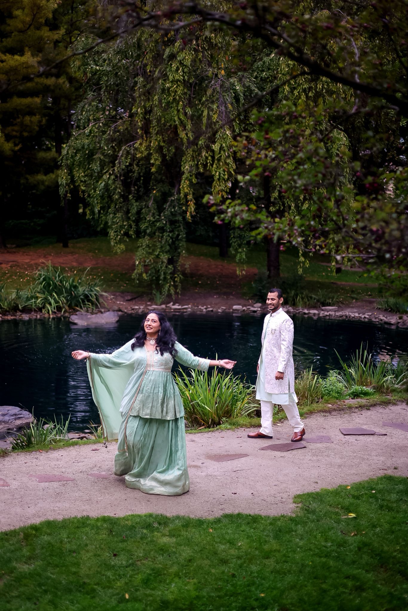 A couple in coordinated outfits enjoys a playful moment by a tranquil pond.