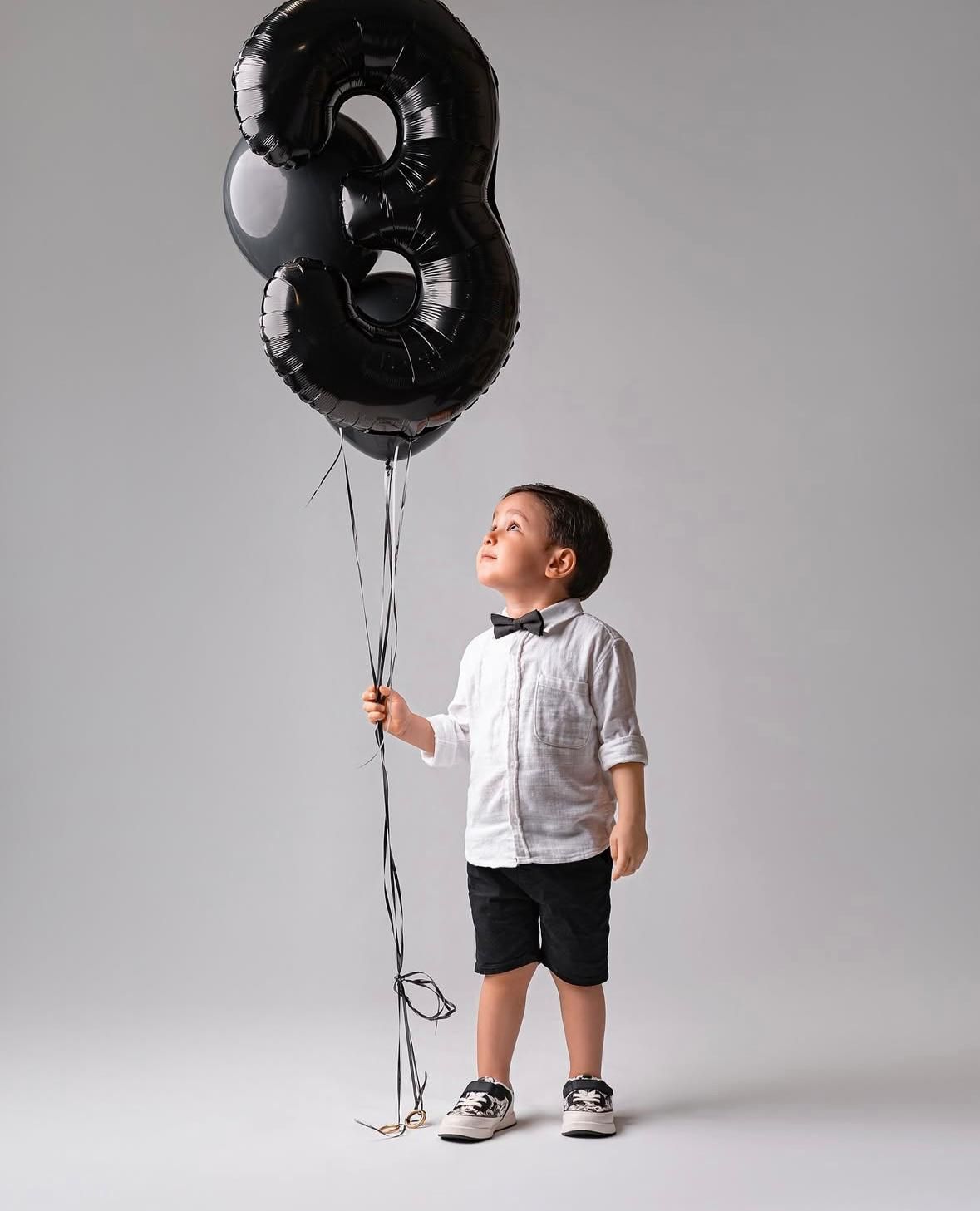 Studio photoshoot with black number balloons against grey background.