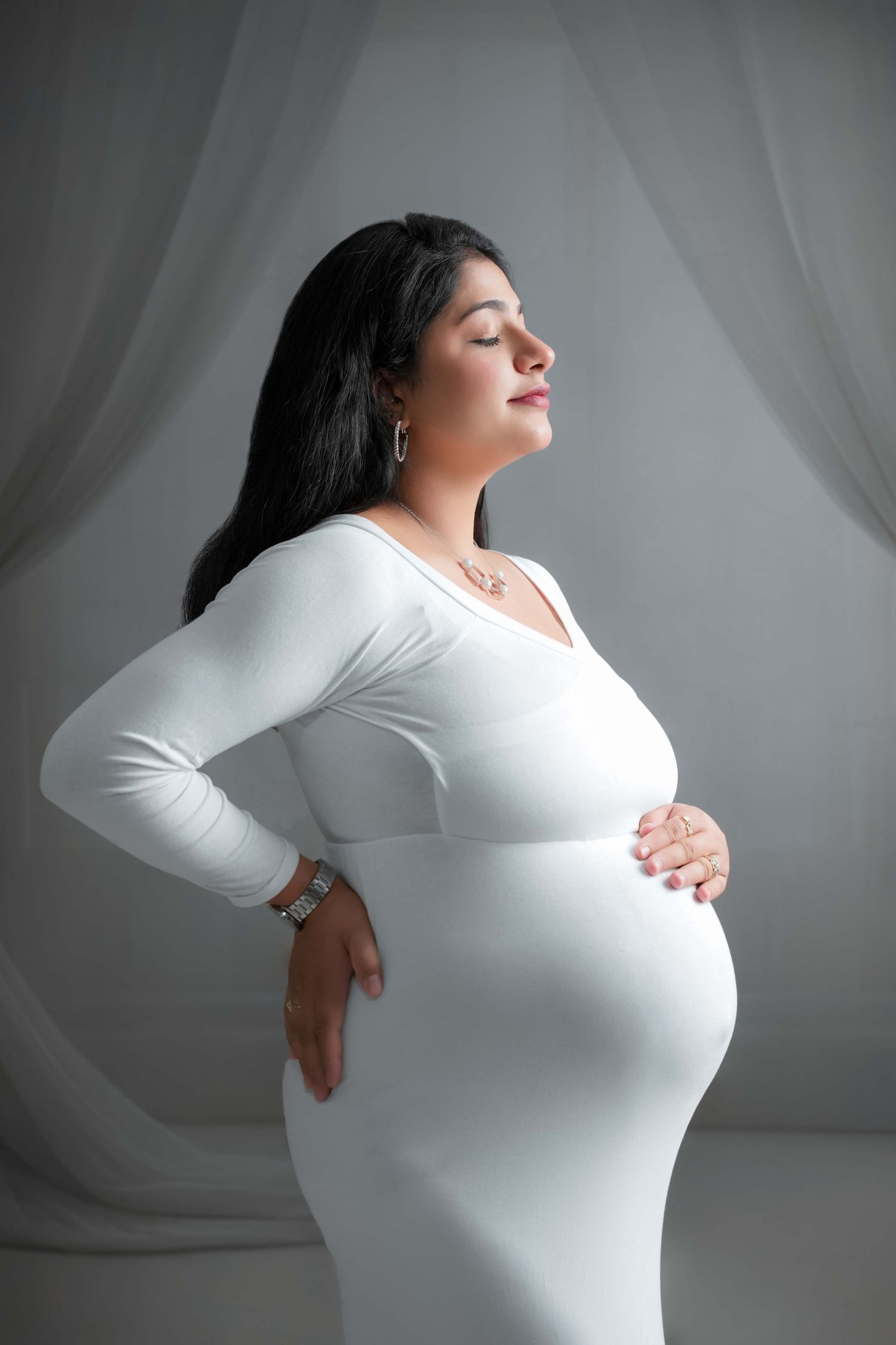 Minimalist maternity portraits in white dress against light backdrop.