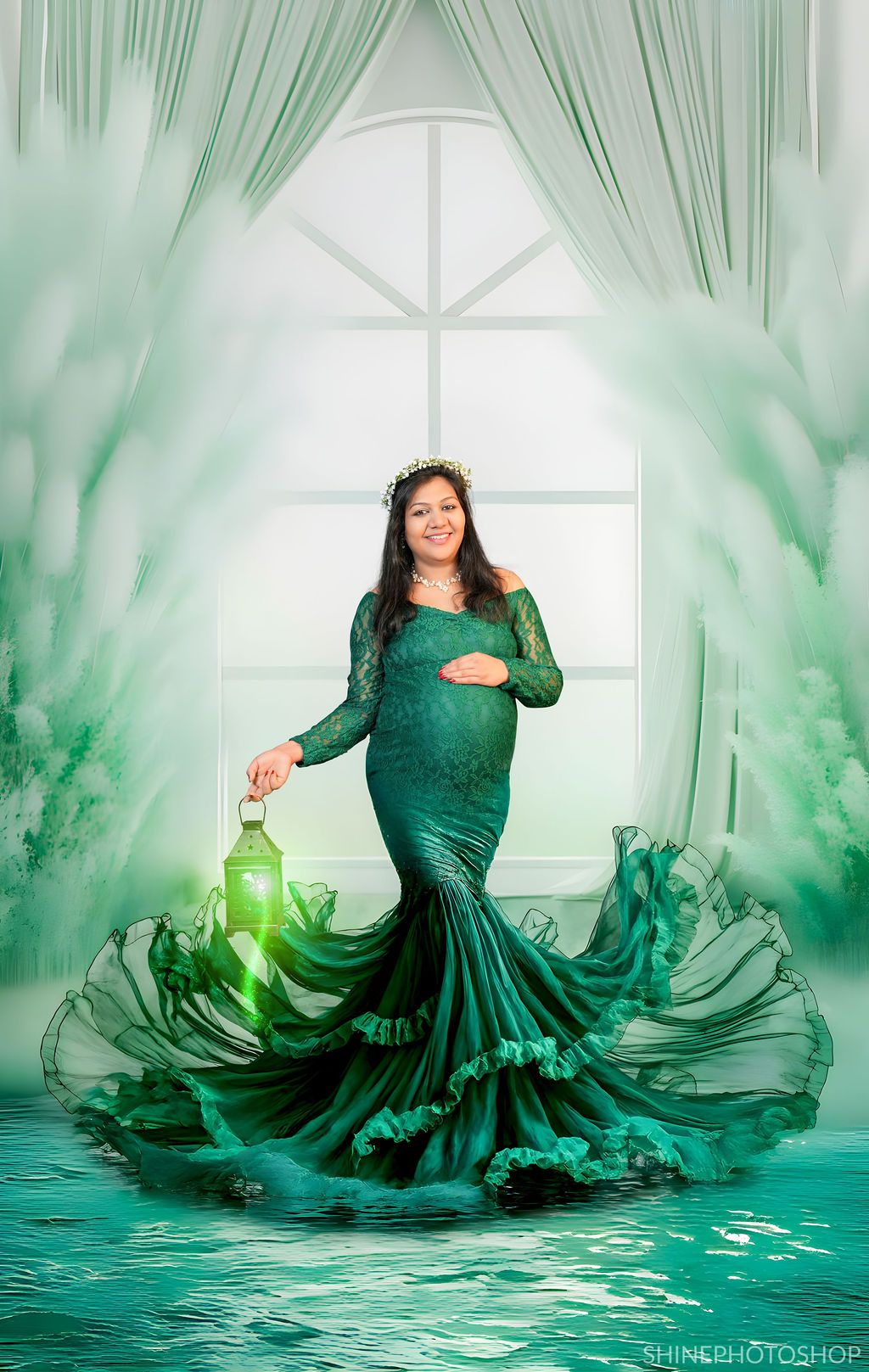 Ethereal maternity photo with flowing emerald dress and glowing lantern in dreamy green setting.