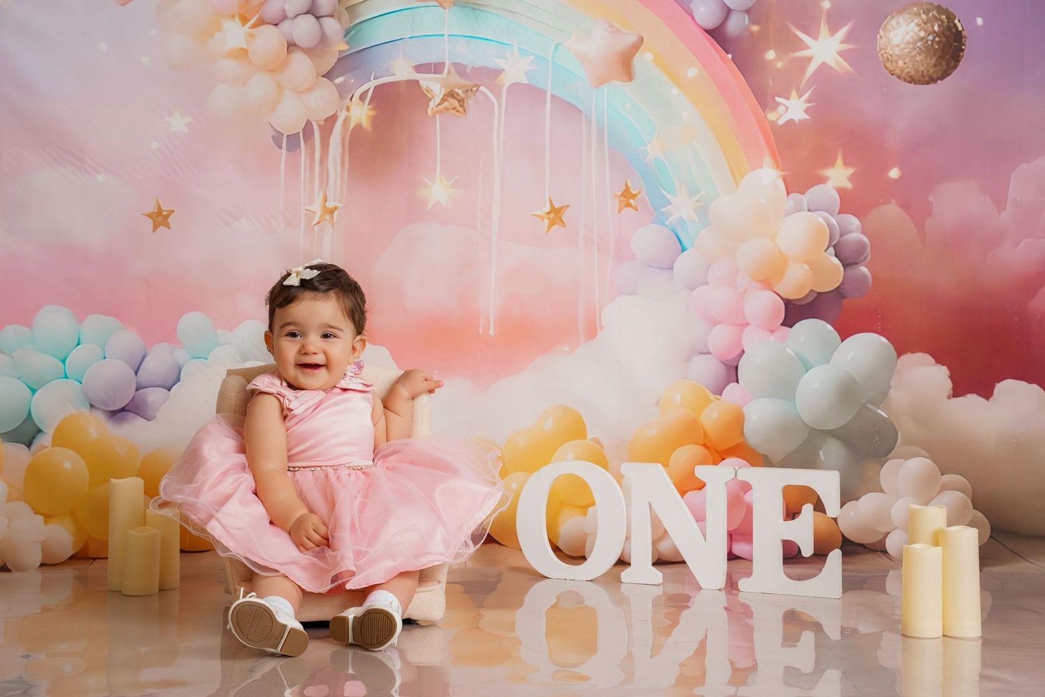 Baby's first birthday scene with 'ONE' letters and pastel pink decorations against rainbow backdrop.