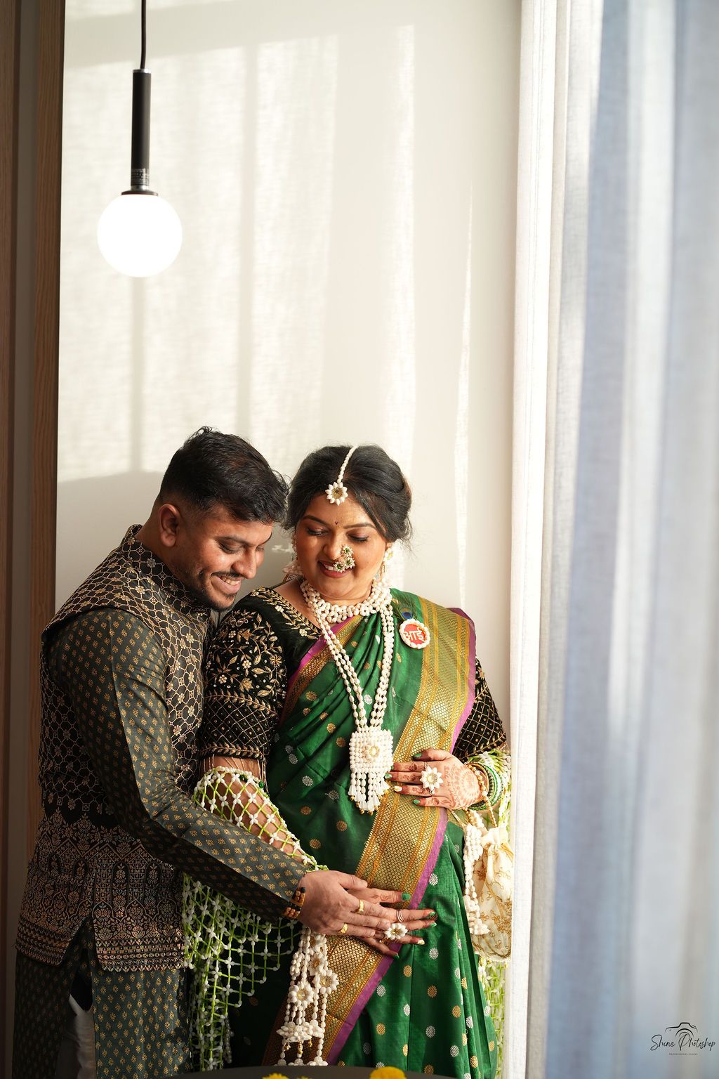 Indian couple in traditional wedding attire, bride in green silk saree with gold jewelry, groom in embroidered sherwani.
