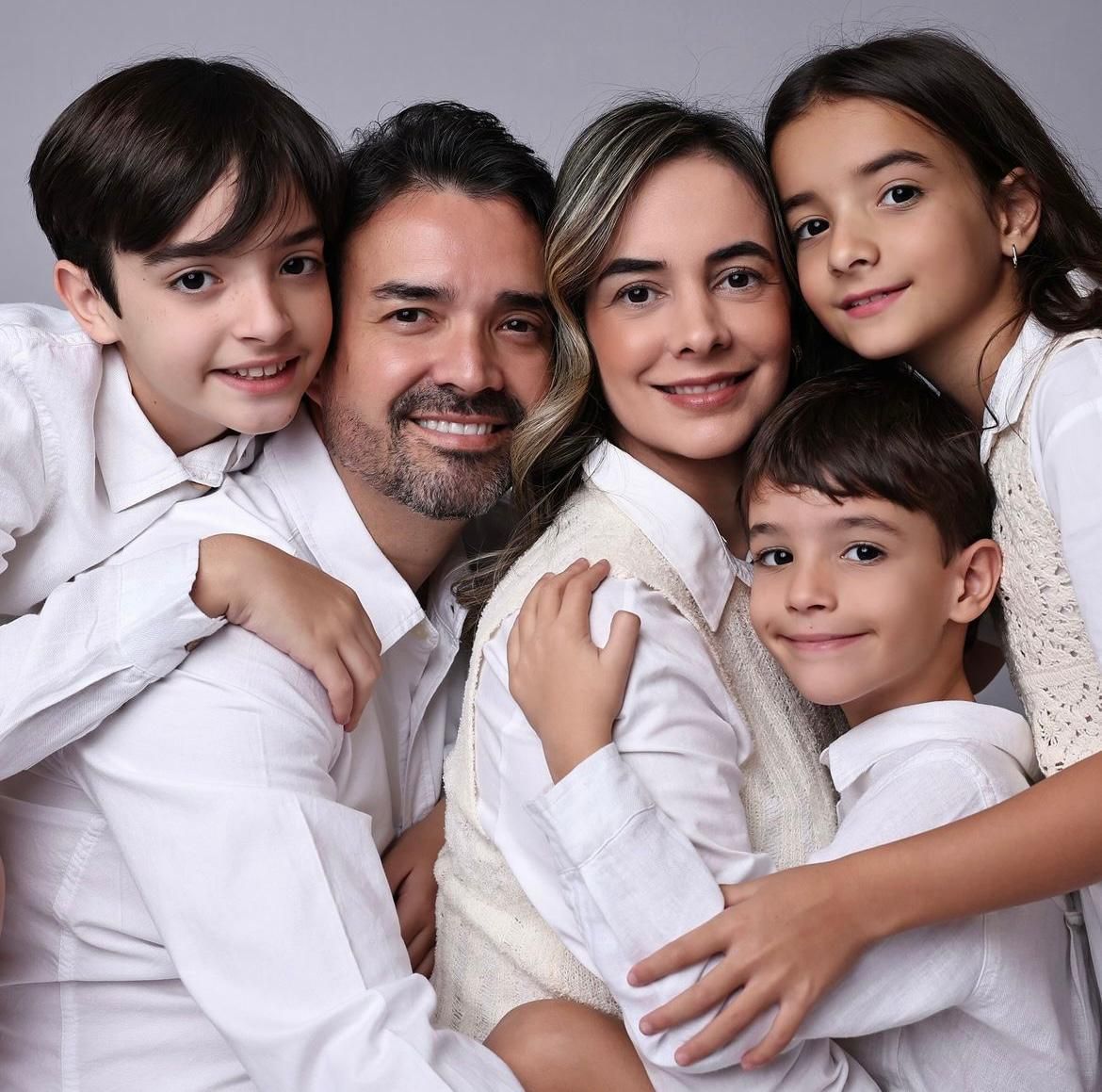 Candid family portrait with everyone dressed in white against grey background.