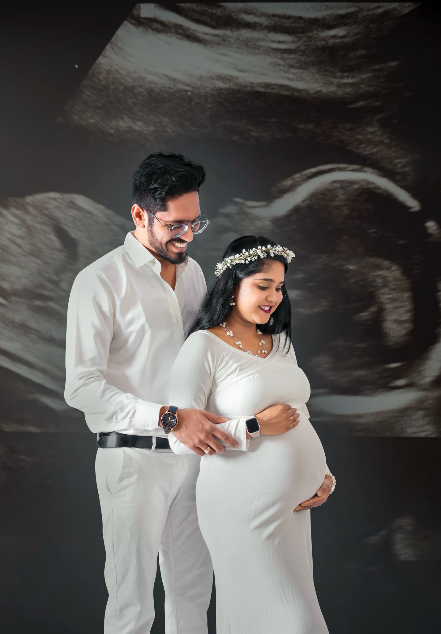 Maternity photo featuring couple in white outfits against ultrasound scan background.