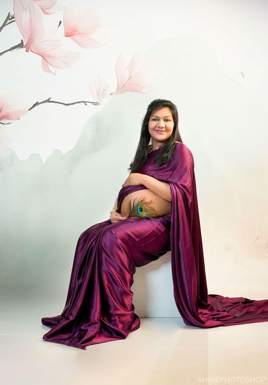 Artistic maternity portraits in a deep purple dress with soft pink floral backdrop.