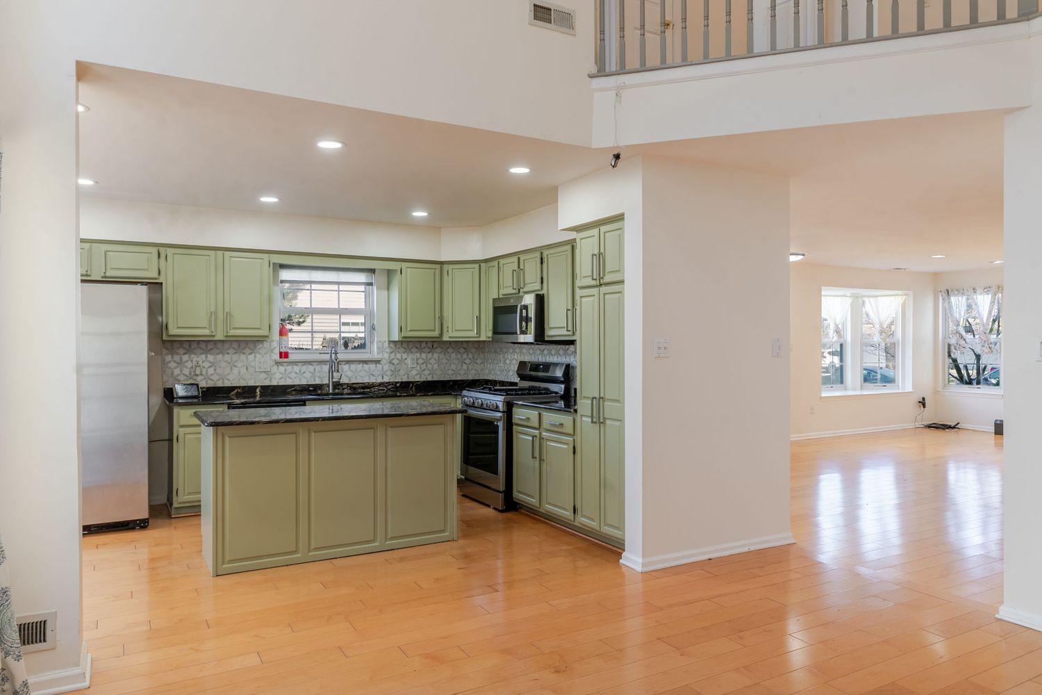 Modern kitchen with green cabinets, dark granite countertops, stainless steel appliances, and hardwood floors.