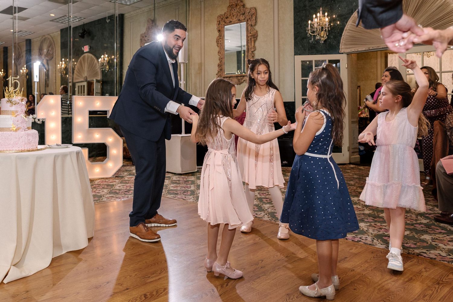 Guests dancing and celebrating at an elegant indoor event with chandeliers and pink decor.