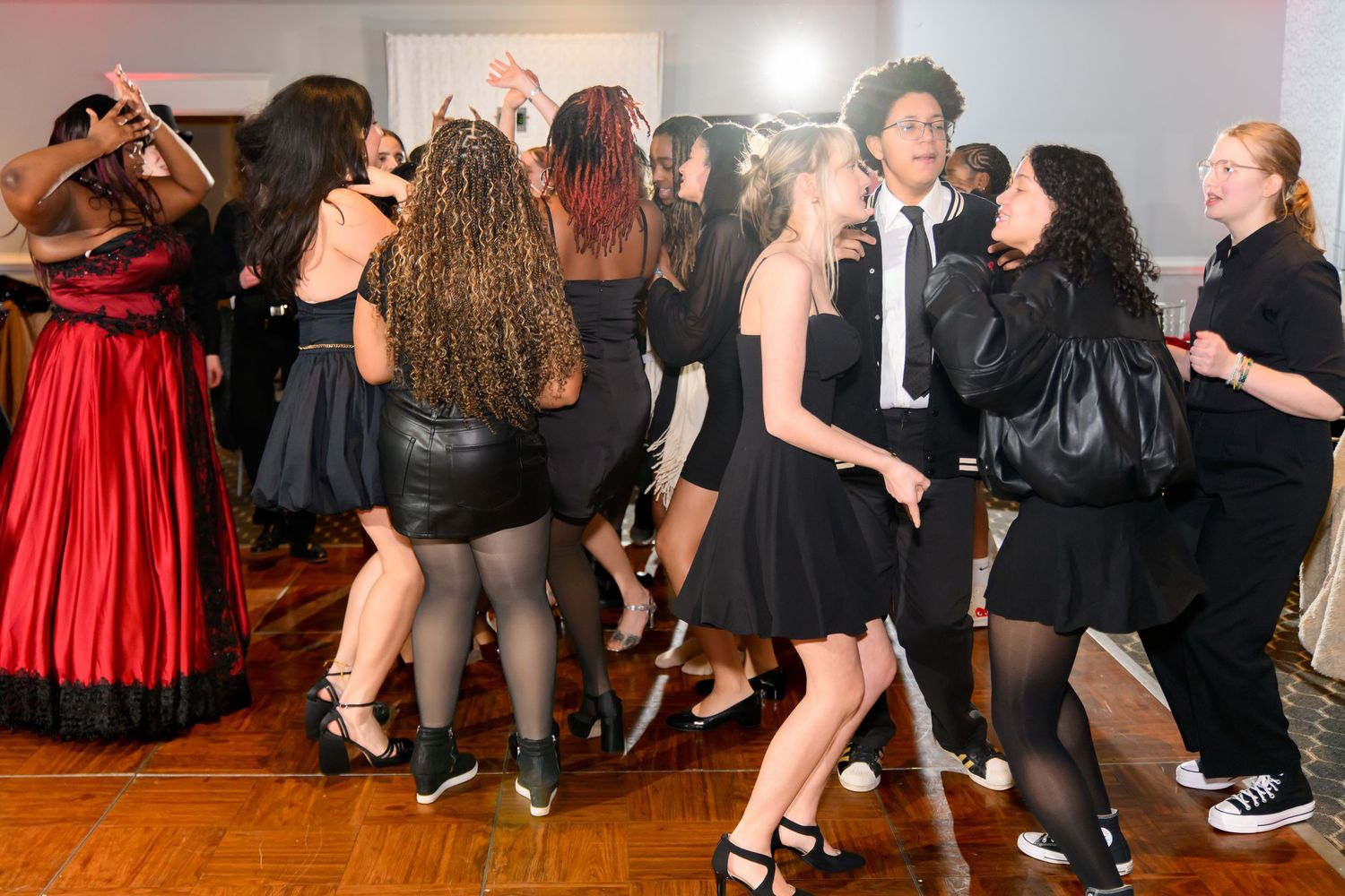 Teens in black outfits dance together at a formal party event on a wooden dance floor.