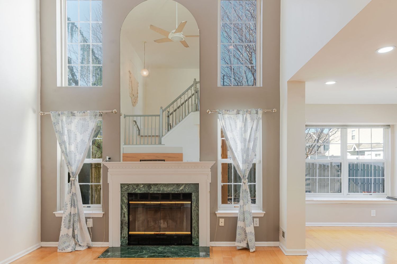 Elegant living room with marble fireplace, soaring ceilings, arched windows, and staircase visible through decorative arch.