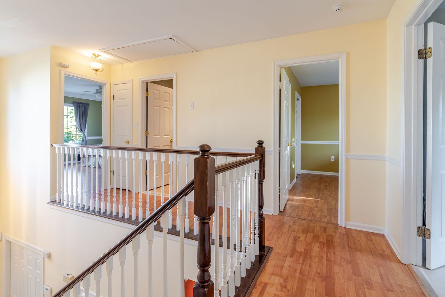 Bright upstairs hallway with hardwood floors, white spindle railing, and open doorways leading to multiple rooms.